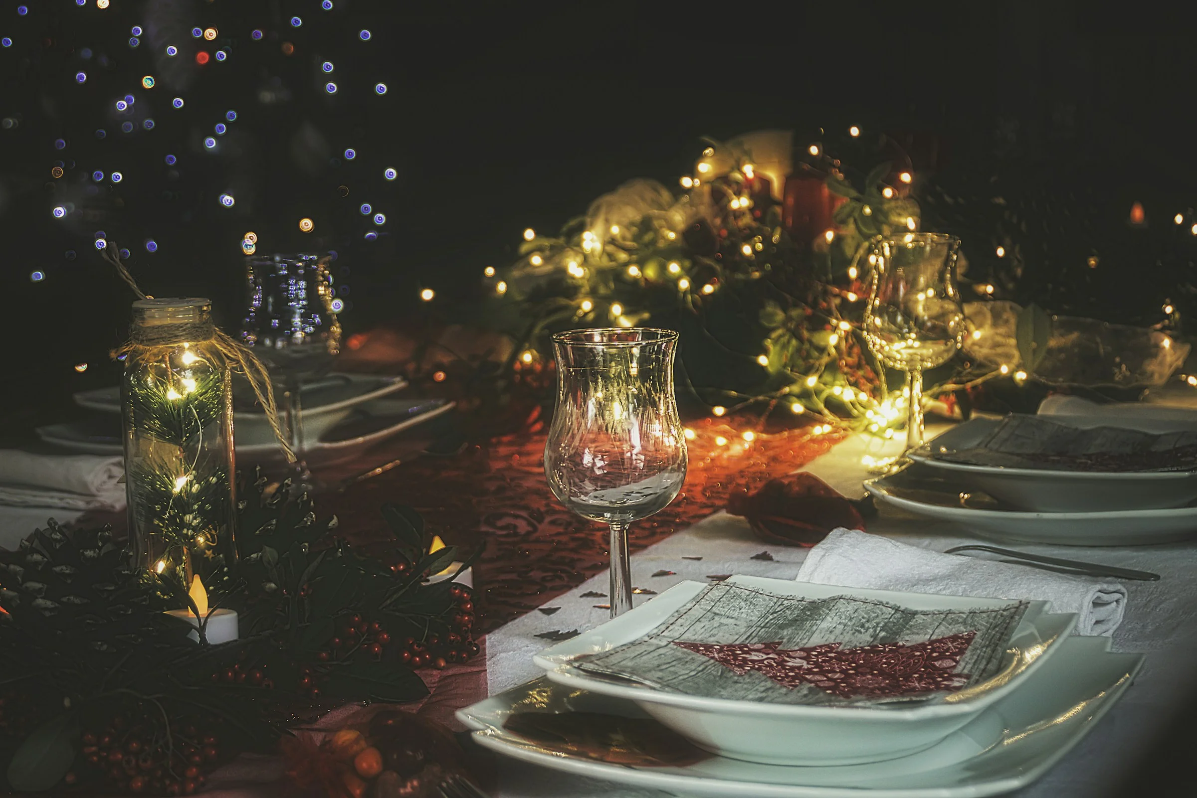 Festively set dinner table with candlelight and glassware for a three-course winter holiday dinner