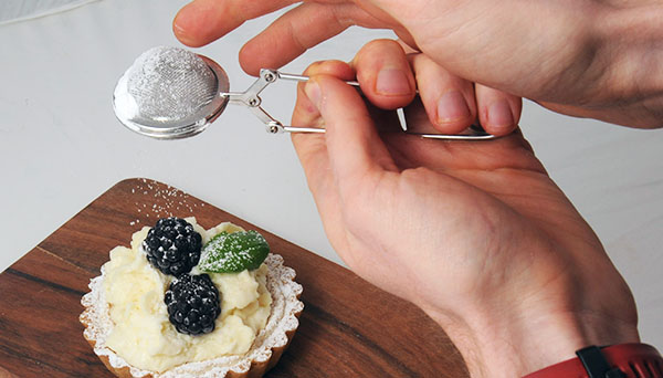 Icing sugar being dusted over a blackberry tartlet